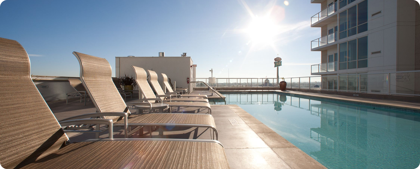 Swimming pool with lounge chairs on the roof of a building, surrounded by a fence
