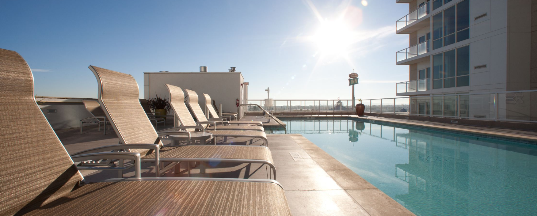Swimming pool with lounge chairs on the roof of a building, surrounded by a fence