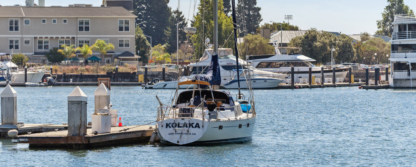 Sailboat docked at a dock with other boats in the water, surrounded by poles, traffic cones, and other objects